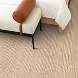 Bedroom setting with white upholstered bench atop a carpet with a subtle stripe pattern in cream and rose red.
