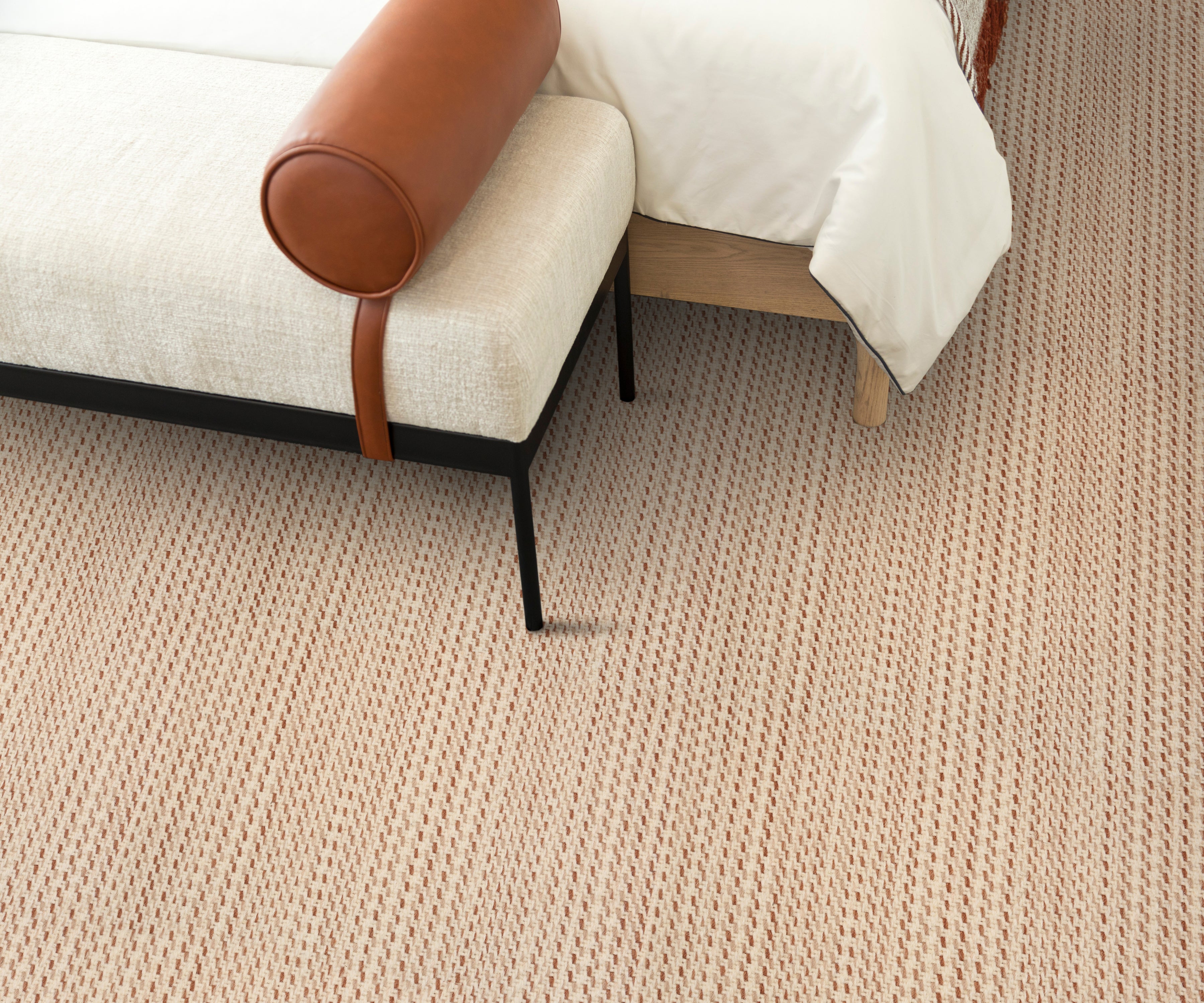 Bedroom setting with white upholstered bench atop a carpet with a subtle stripe pattern in cream and rose red.