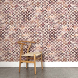 A wooden chair stands in front of a wall papered in a painterly small-scale diamond print in cream, brown, purple and pink.