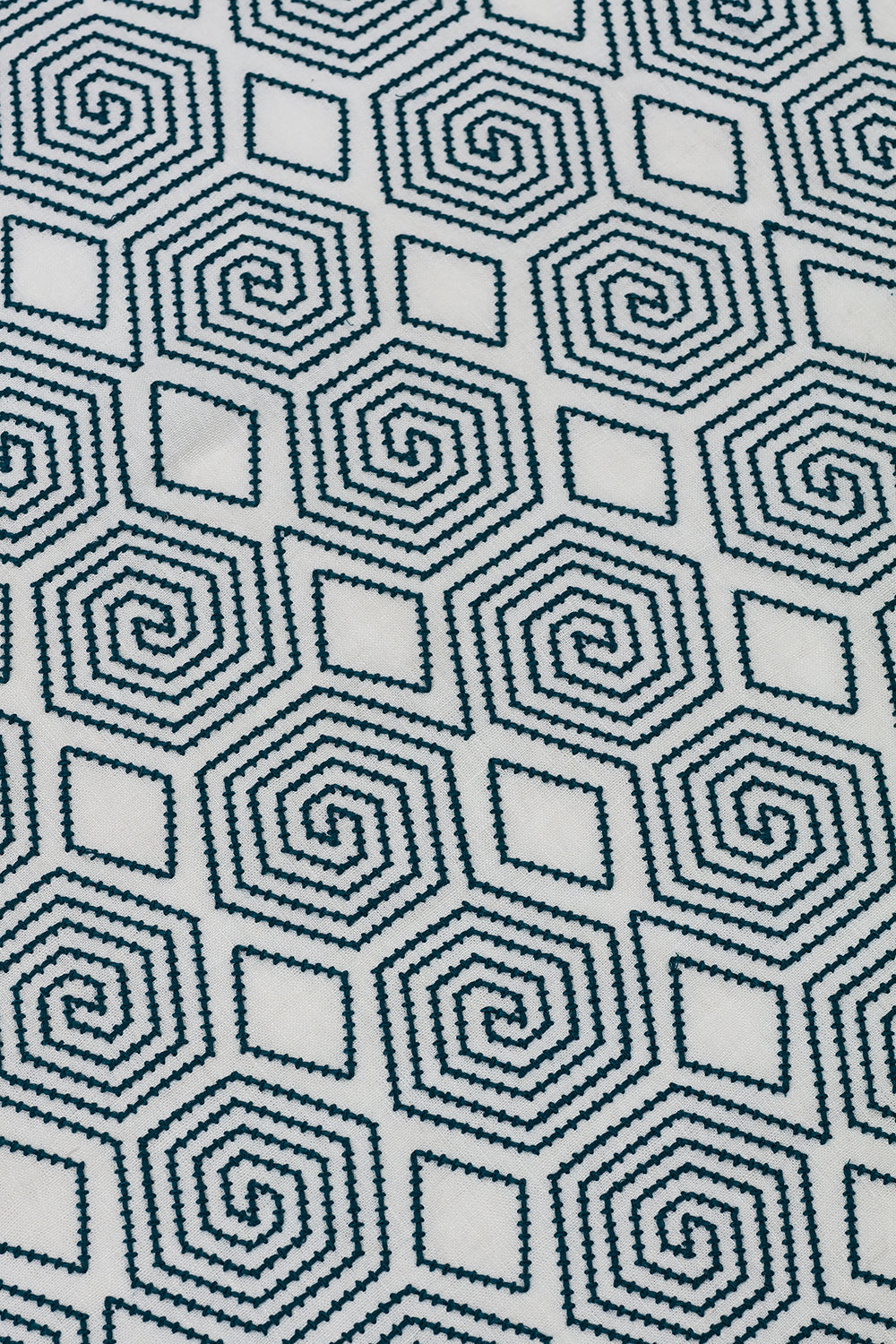 Detail of an embroidered fabric in a geometric spiral design in navy on a cream field. 