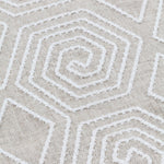 Detail of fabric with a playful embroidered geometric grid print in white on a cream field.
