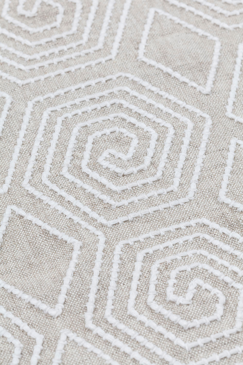 Detail of fabric with a playful embroidered geometric grid print in white on a cream field.