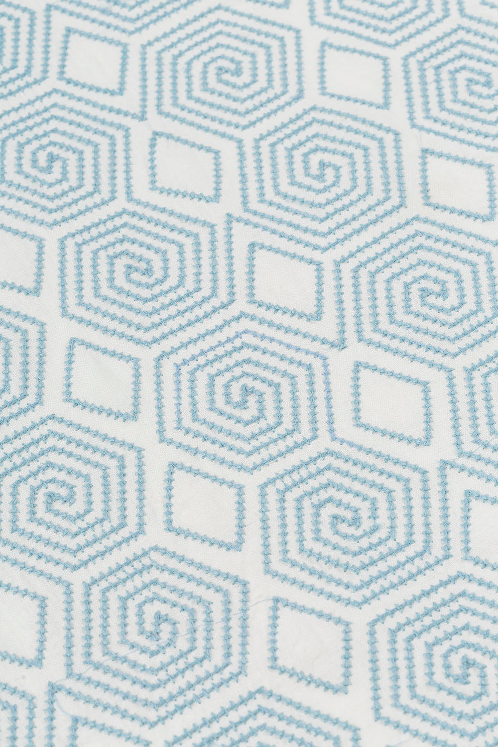 Detail of fabric with a playful embroidered geometric grid print in light blue on a white field.