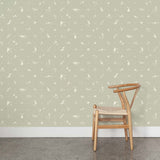 A wooden chair stands in front of a wall papered in a playful animal and branch print in white on a sage field.