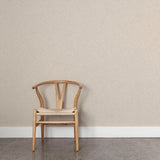 A wooden chair stands in front of a wall papered in a small-scale dot and dash pattern in tan and white on a cream field.
