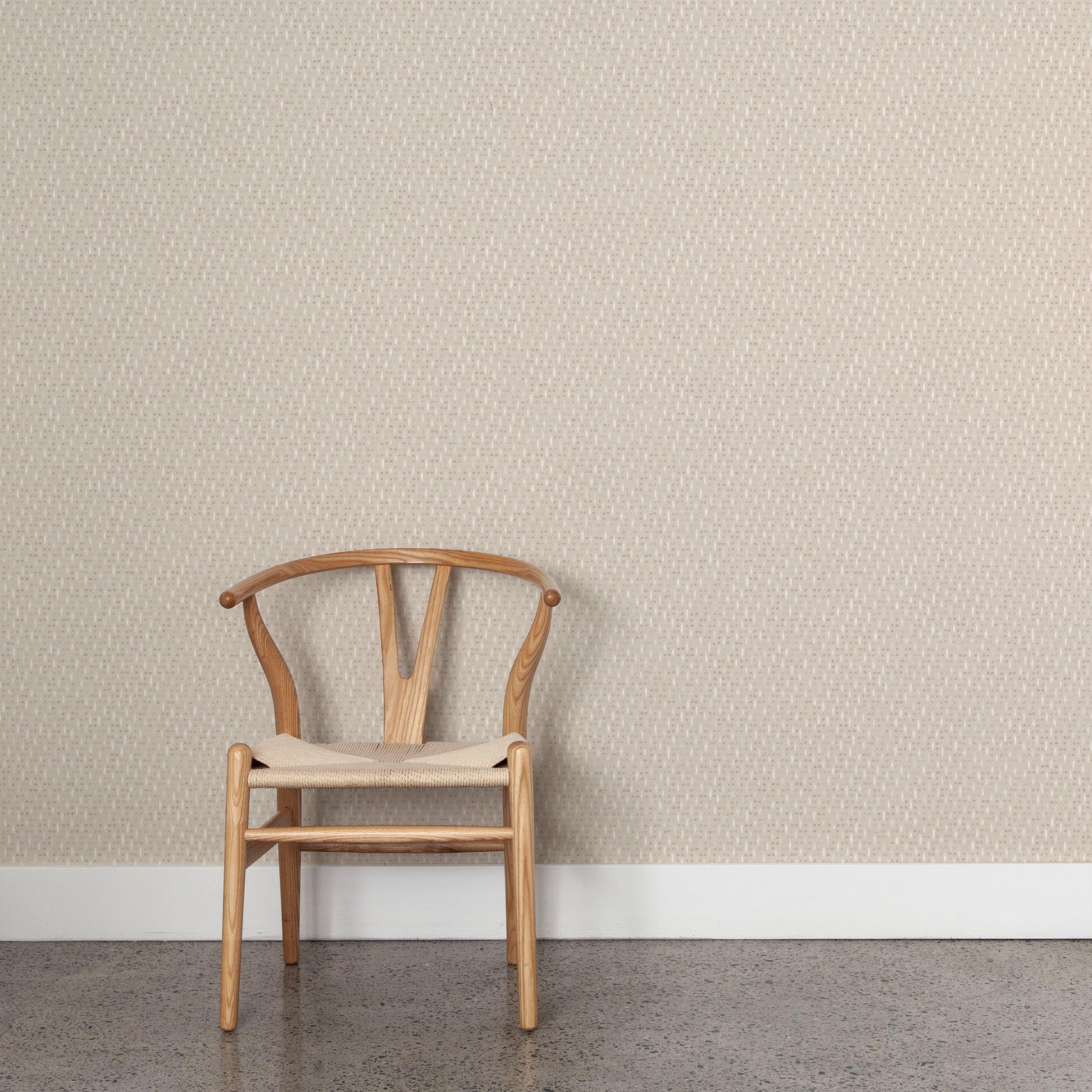 A wooden chair stands in front of a wall papered in a small-scale dot and dash pattern in tan and white on a cream field.