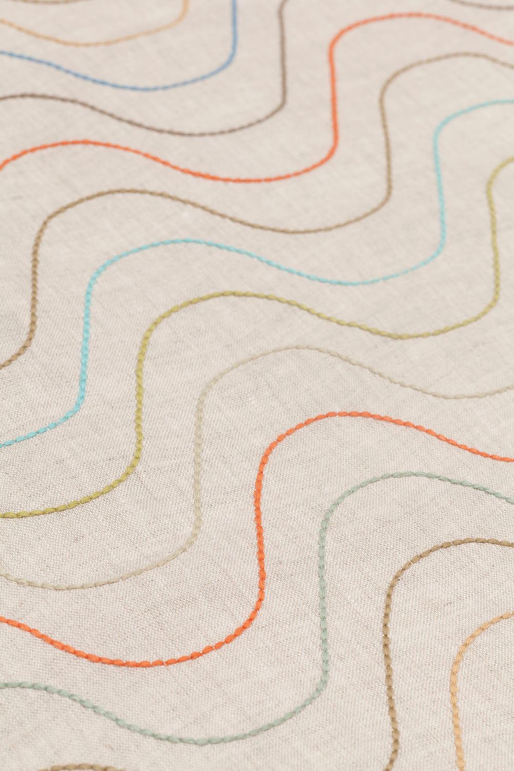Detail of fabric with an embroidered undulating stripe pattern in shades of yellow, red and blue on a cream field.
