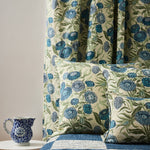 Bedrooms scene with checkerboard quility and pillows in a floral orinted linen in a daisy design in shades of blue with green leaves on a pale cream field.