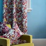 Lime green velvet chair with read and turquoise floral patterns against a matching curtain on a bright blue wall. 