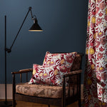 Wooden side chair with floral printed upholstery and pillows against a teal wall, with a curtain in the same floral design. 