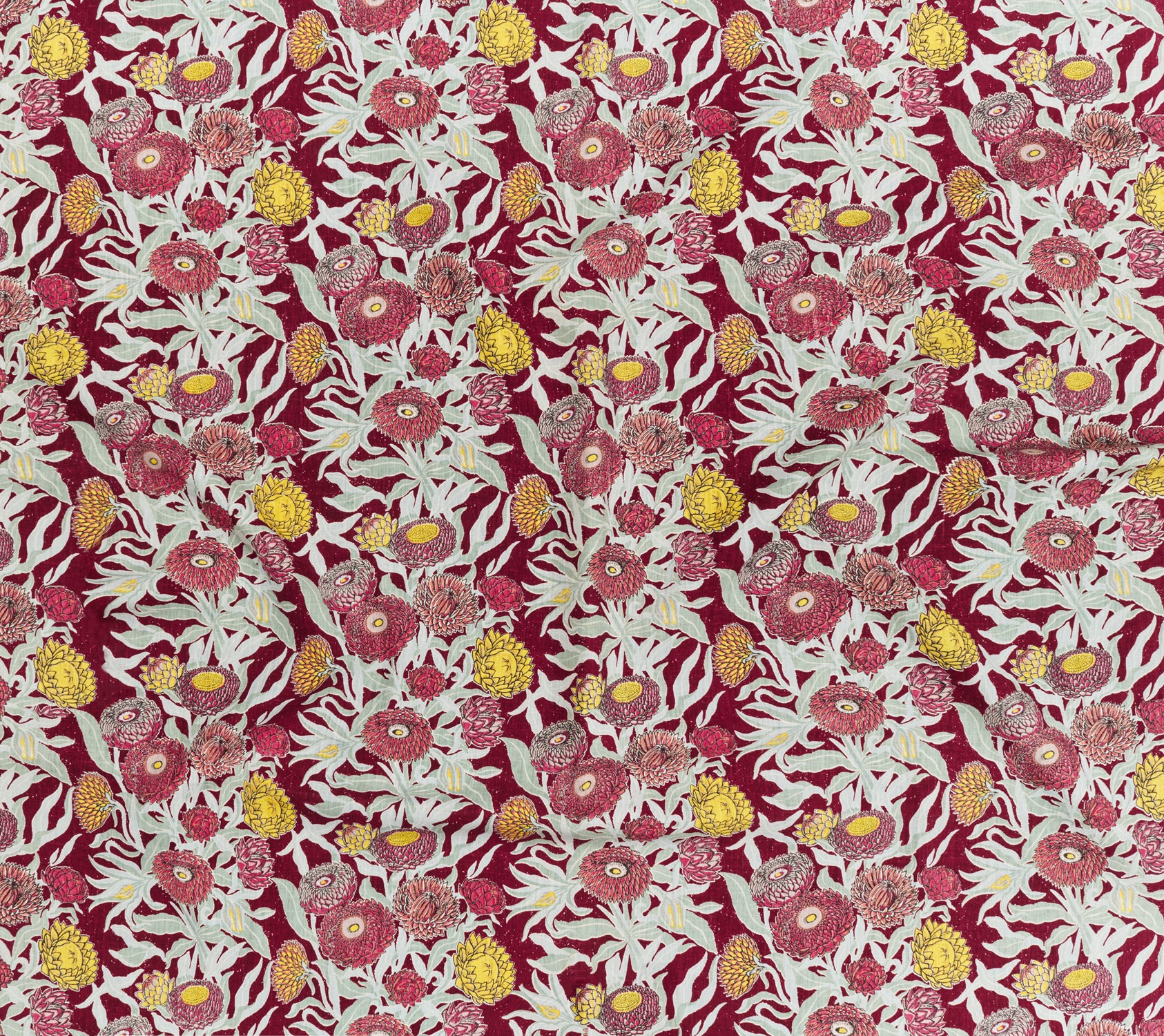Printed linen in a hand drawn daisy design in shades of red, pink and yellow with sage leaves on a crimson field.