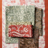 A mood board flat lay with patterned fabric in assorted botanical prints in shades of pink, brown, blush and red on a solid orange background.