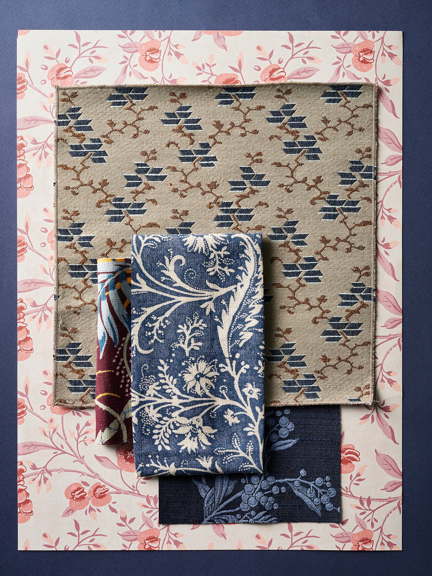A styled flat-lay of fabric and wallpaper swatches in an array of floral and botanical patterns in blue, beige, pink and cream. 