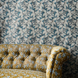 A close-up of a tufted couch upholstered in mustard brown fabric with a light blue floral pattern, set against a fabric  backdrop in a blue and white leaf motif