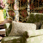 Green upholstered chair with floral patterned cushions in a room with floral curtains.