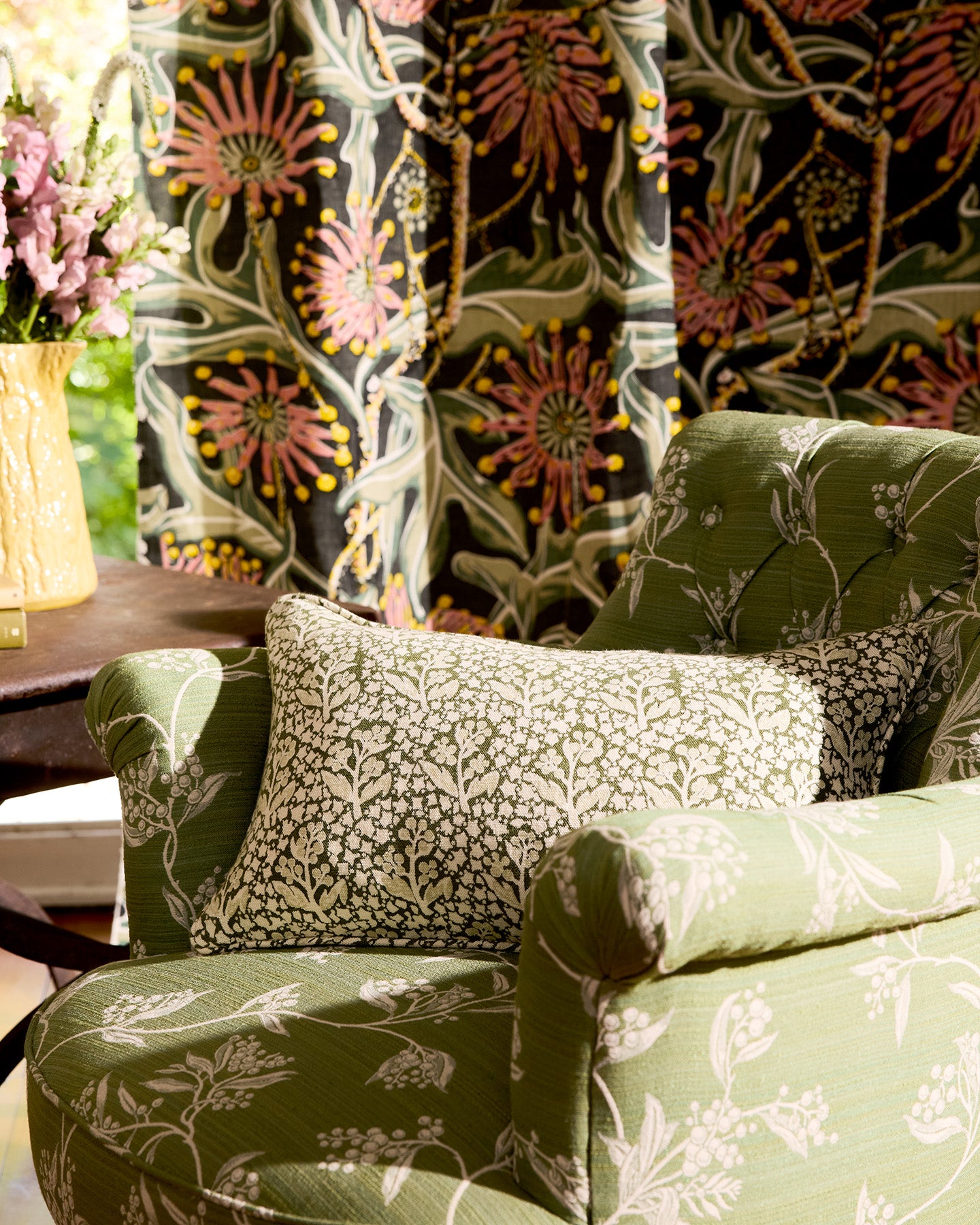 Green upholstered chair with floral patterned cushions in a room with floral curtains.