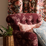 Decorative armchair with floral pattern in a room with floral curtains and a plant.
