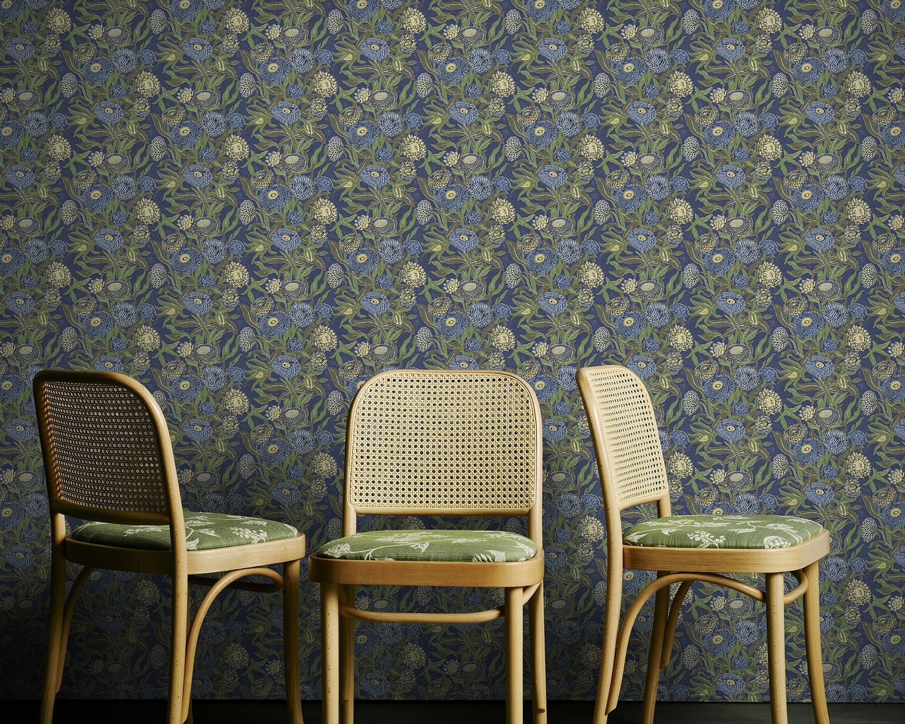 Three wicker chairs with green cushions against a floral wallpapered wall.