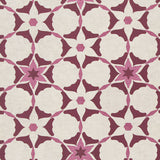 Detail of fabric in a geometric star print in shades of pink and maroon on a cream field.