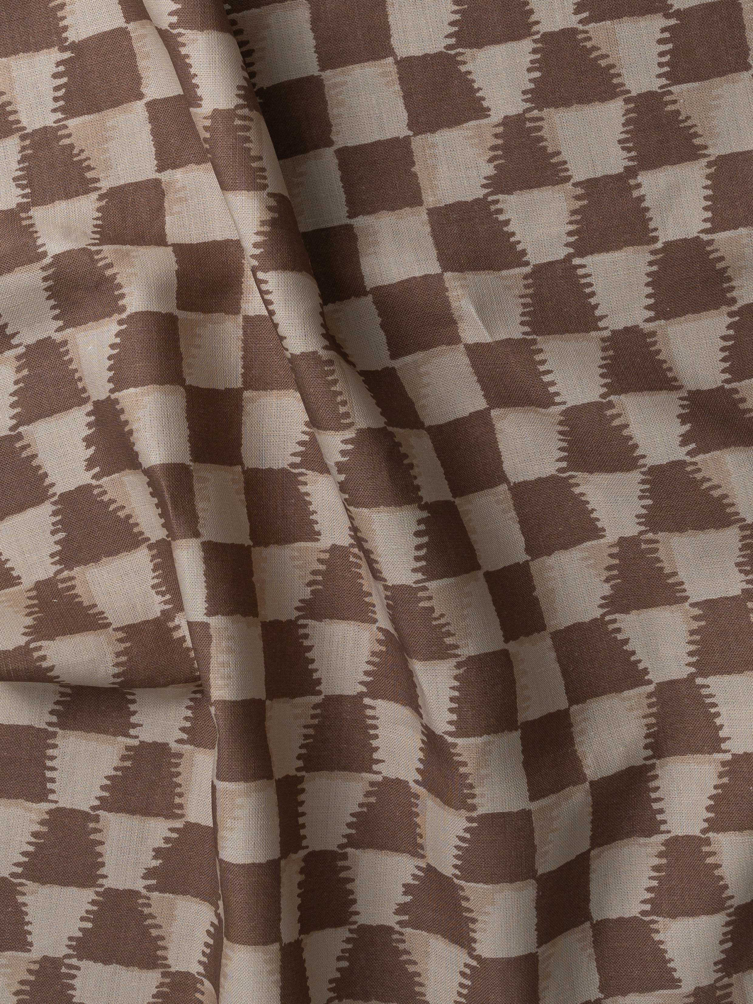 Detail of gently draped printed fabric in a watercolor ikat-inspired checkerboard pattern in tonal warm clay brown. 