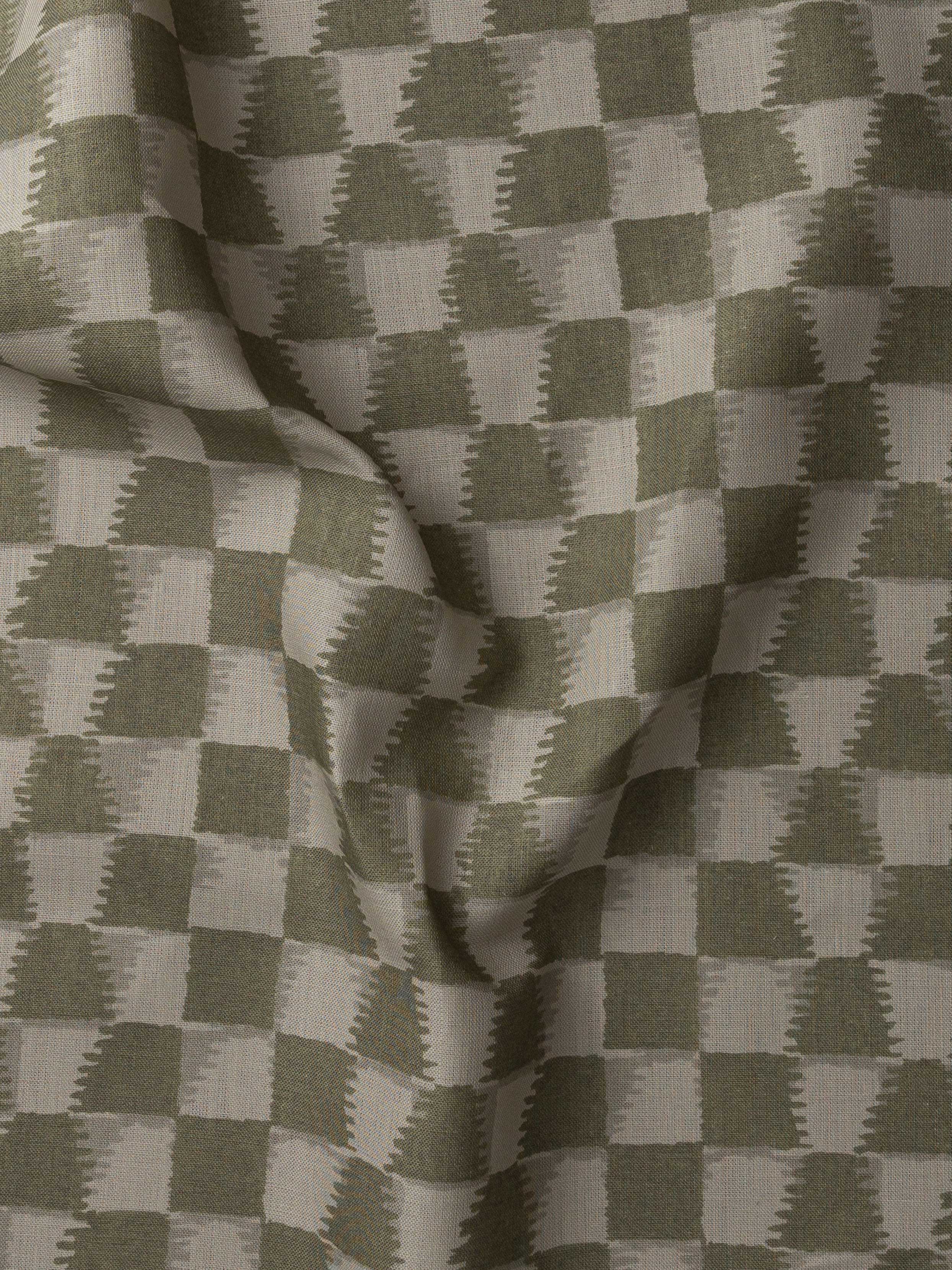 Detail of gently draped printed fabric in a watercolor ikat-inspired checkerboard pattern in tonal muted olive green.