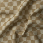 Detail of gently draped printed fabric in a watercolor ikat-inspired checkerboard pattern in warm tan.