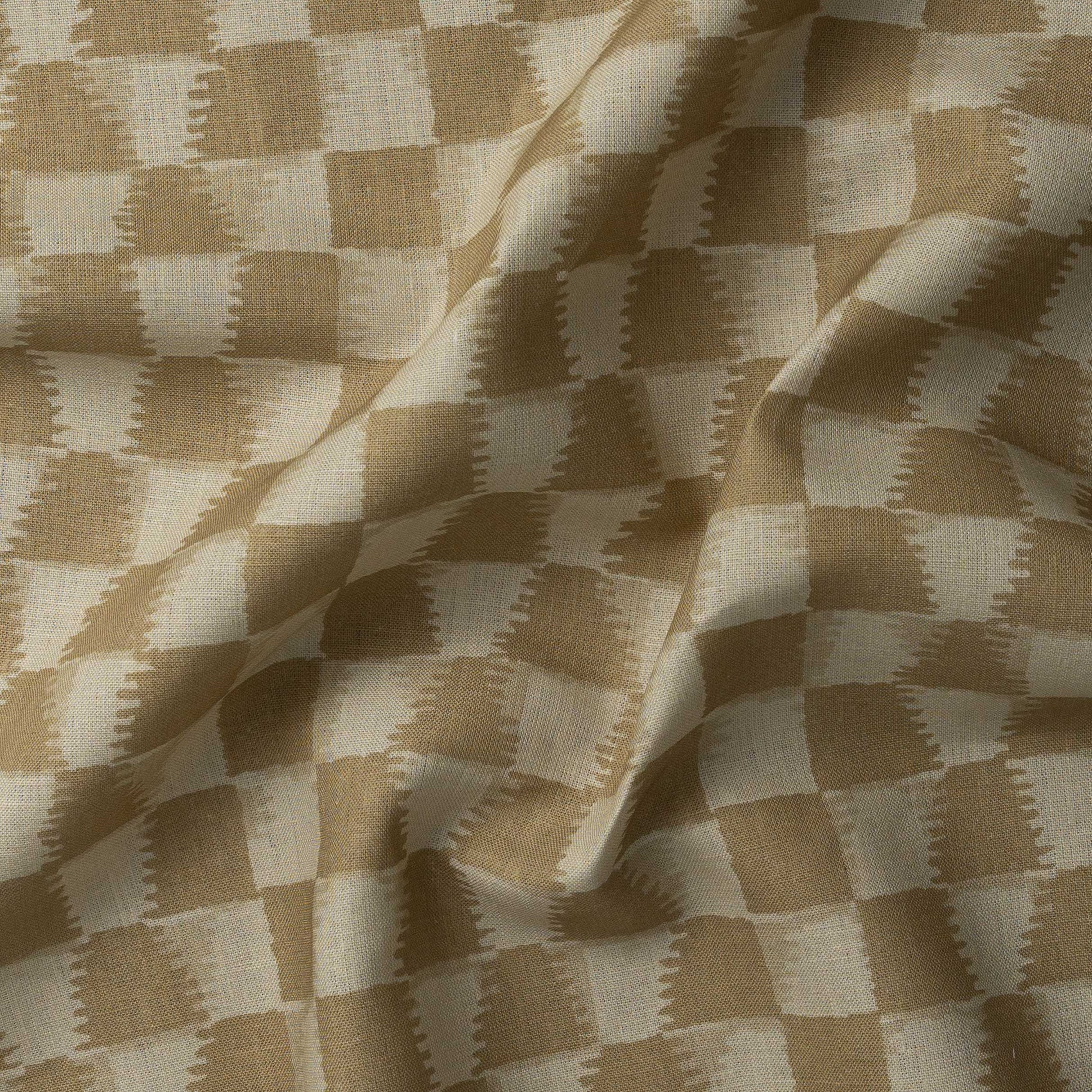 Detail of gently draped printed fabric in a watercolor ikat-inspired checkerboard pattern in warm tan.