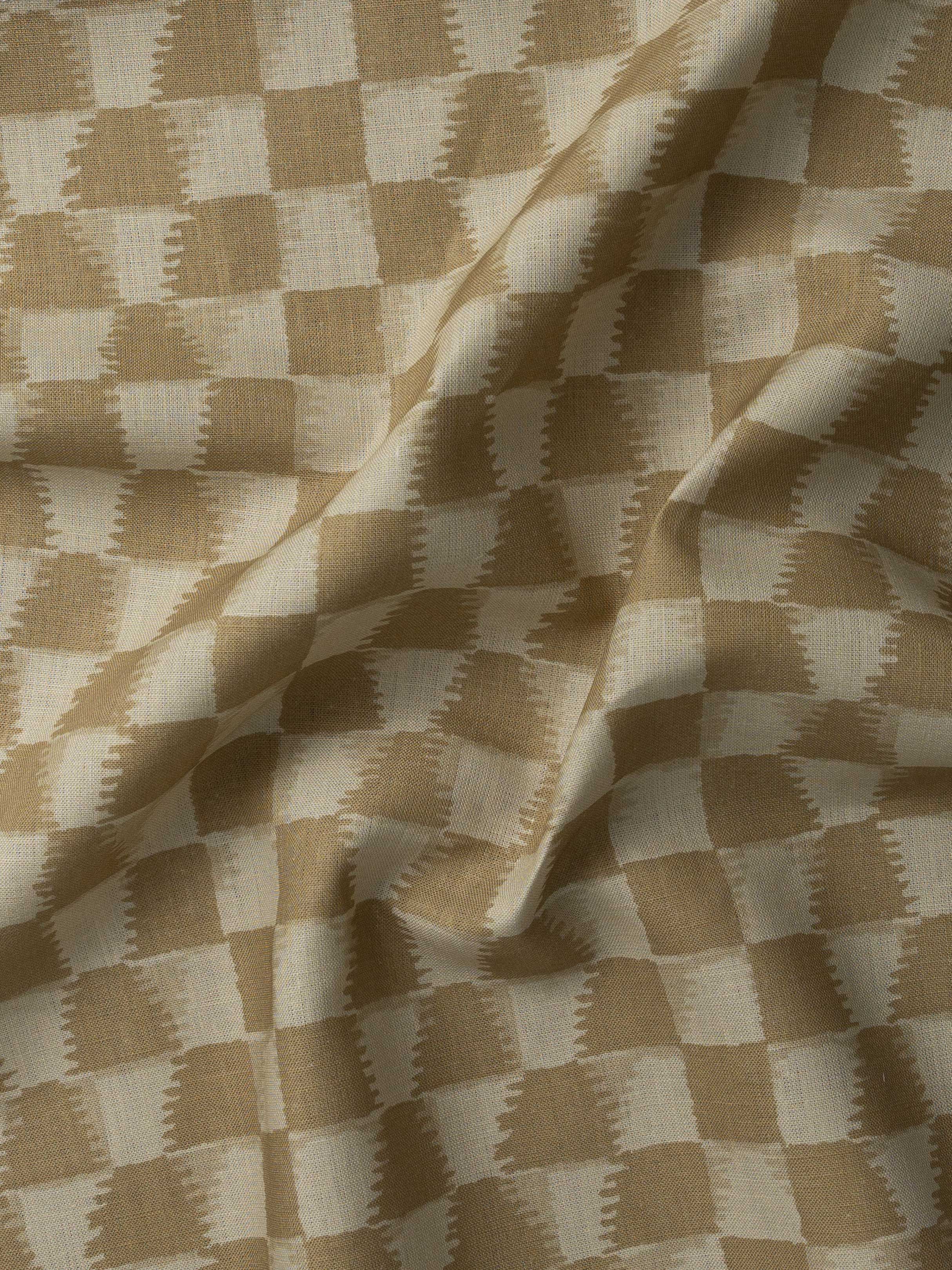 Detail of gently draped printed fabric in a watercolor ikat-inspired checkerboard pattern in warm tan.