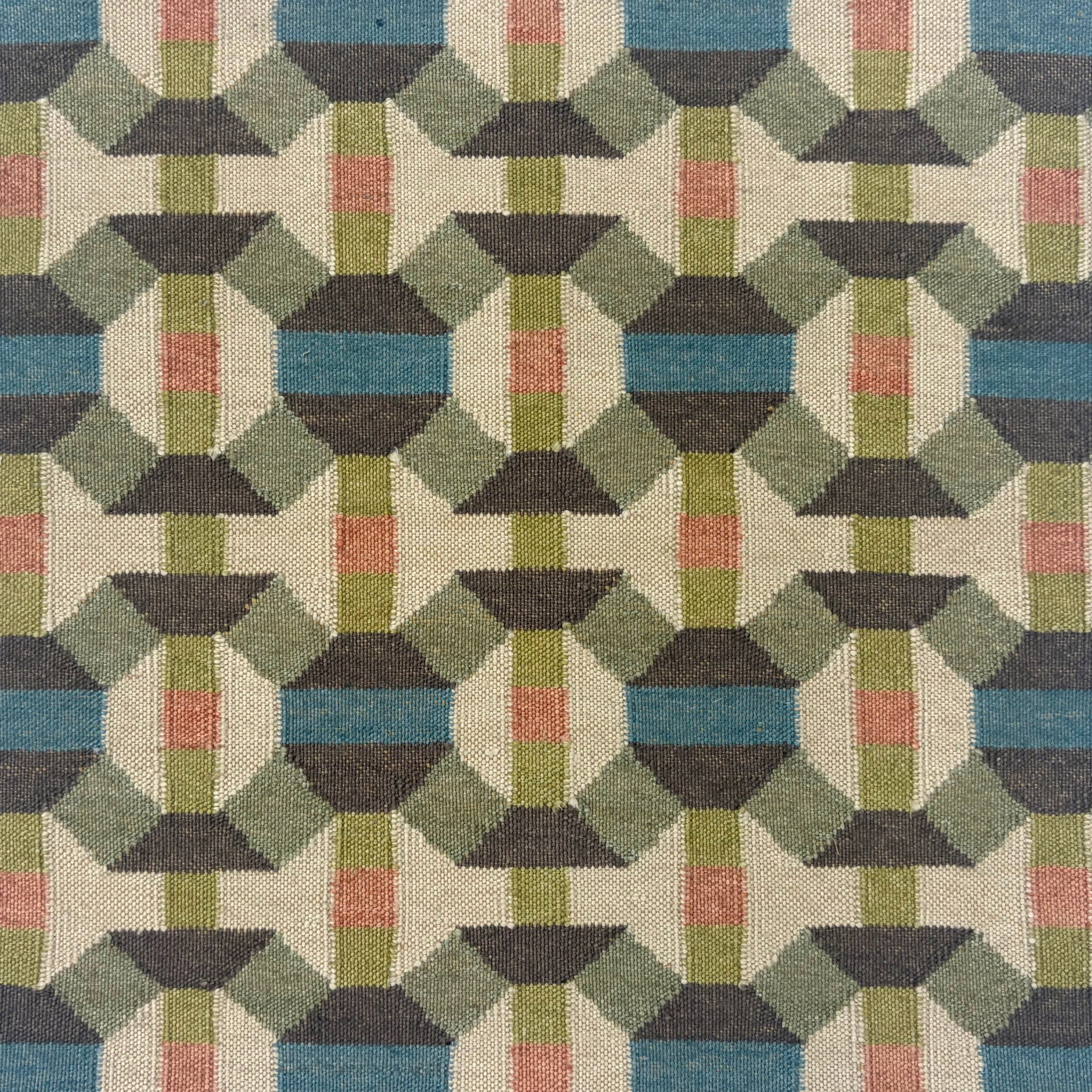 Handmade flatweave rug with complex geometric design in green, charcoal grey, blue, lime green, cream and coral pink.