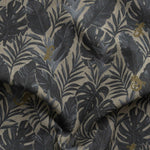 Detail of gently draped printed fabric in a tropical palm frond pattern in muted steel blue scattered with small tan lizards. 