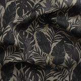 Detail of gently draped printed fabric in a tropical palm frond pattern in faded black and charcoal grey scattered with small tan lizards. 