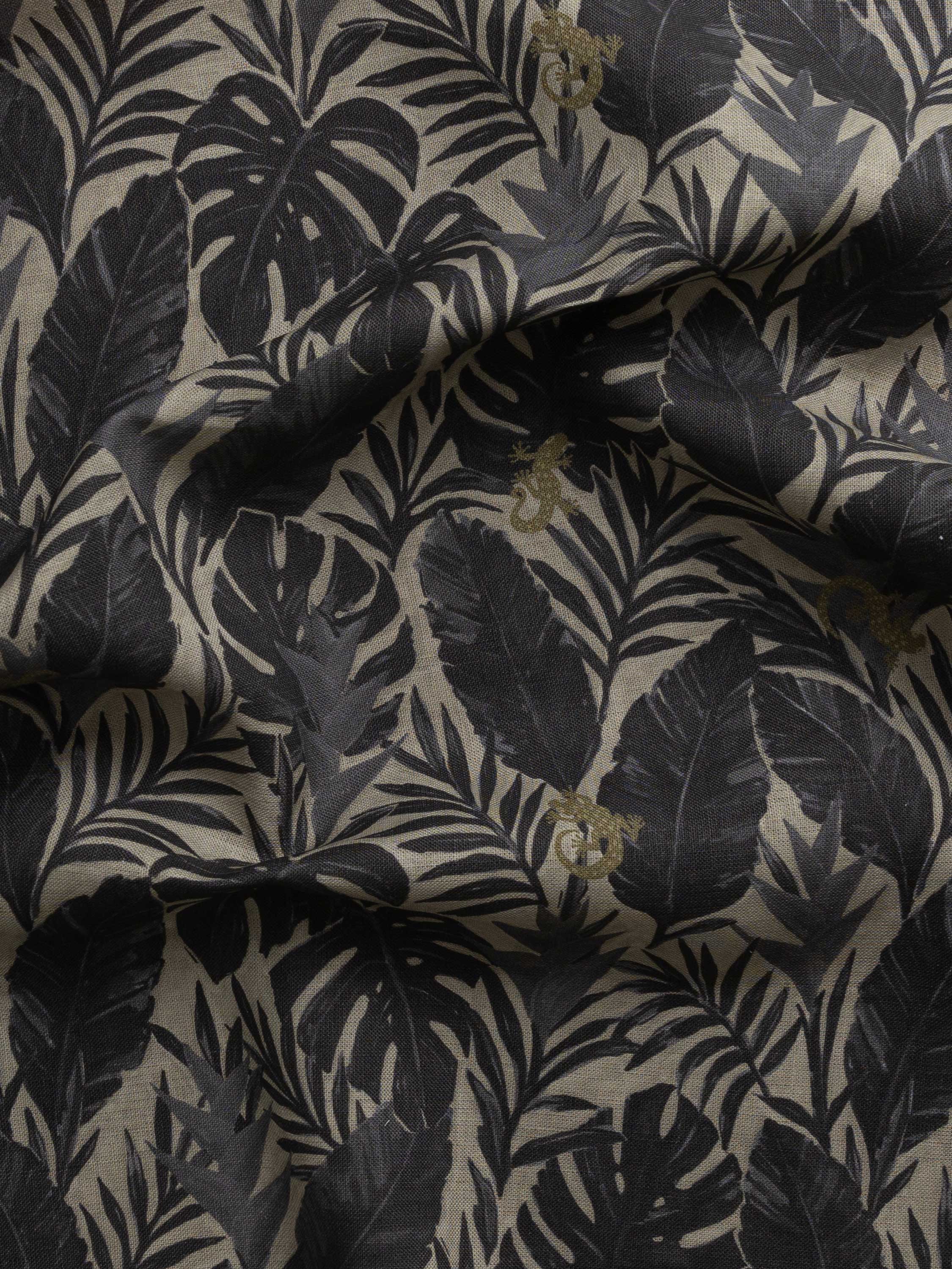 Detail of gently draped printed fabric in a tropical palm frond pattern in faded black and charcoal grey scattered with small tan lizards. 