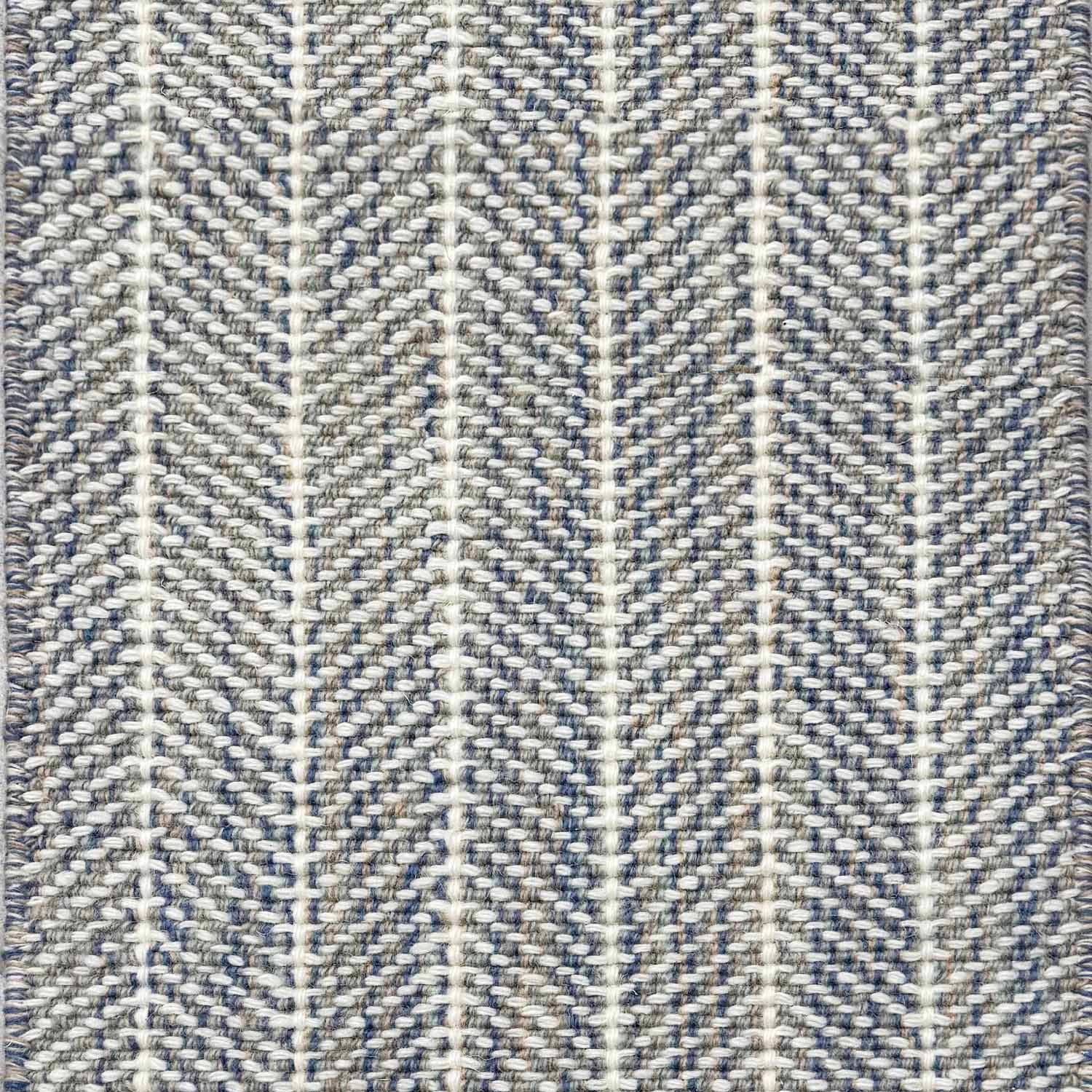 Close up of broadloom carpet with striated herringbone weave in white with accents of blue and brown.