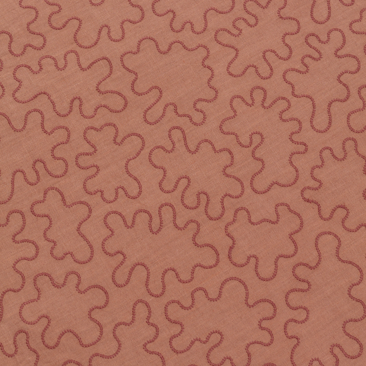 Detail of a wabric with an abstract embroidered pattern in clay pink on a clay pink field.