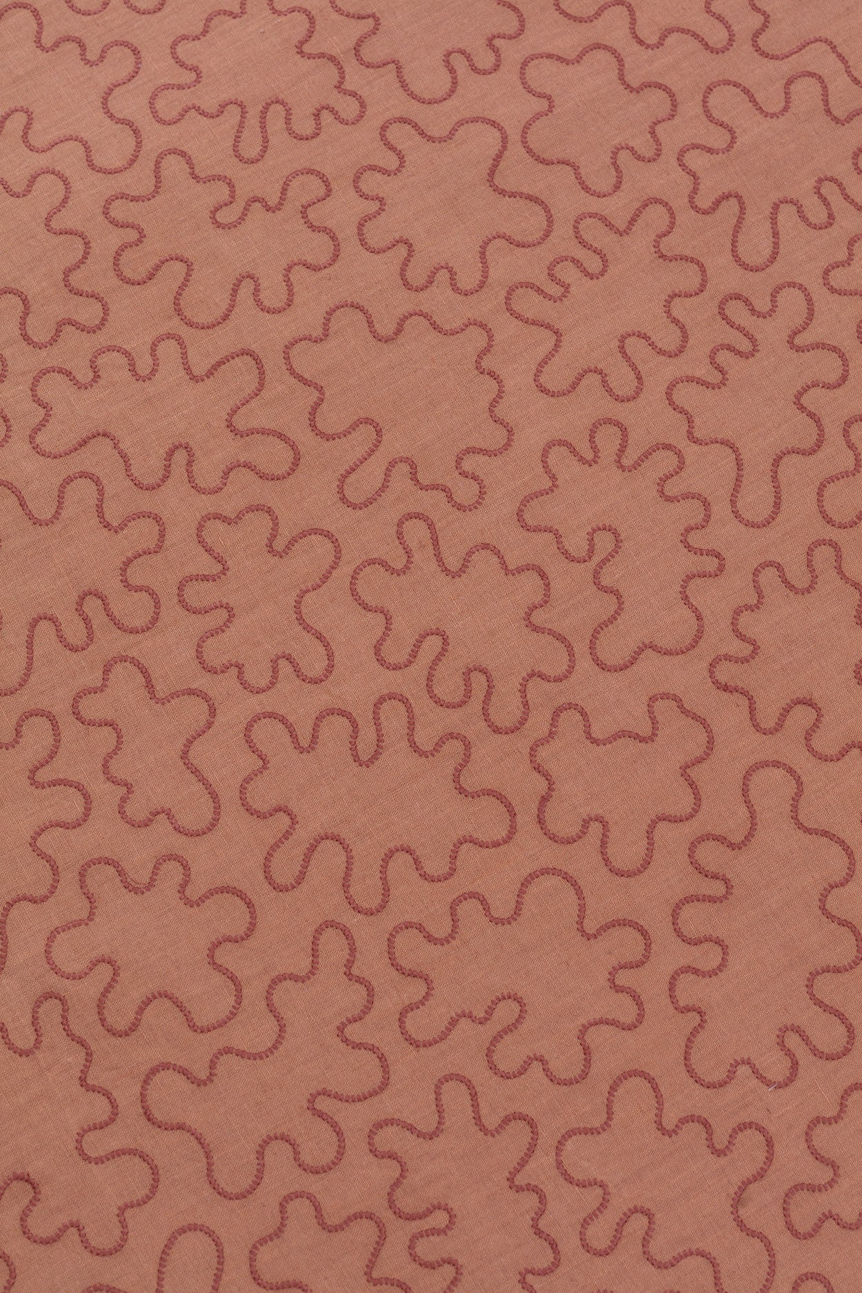 Detail of a wabric with an abstract embroidered pattern in clay pink on a clay pink field.