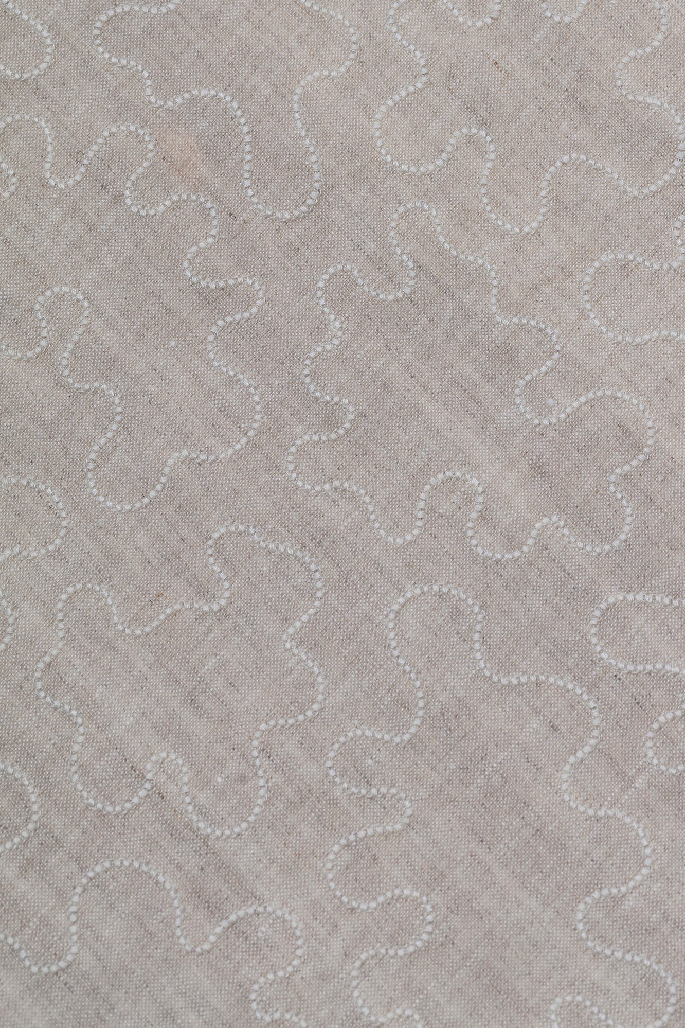 Fabric with an abstract embroidered pattern in white on a cream field.