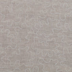 Detail of fabric with an abstract embroidered pattern in white on a cream field.
