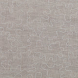 Detail of fabric with an abstract embroidered pattern in white on a cream field.