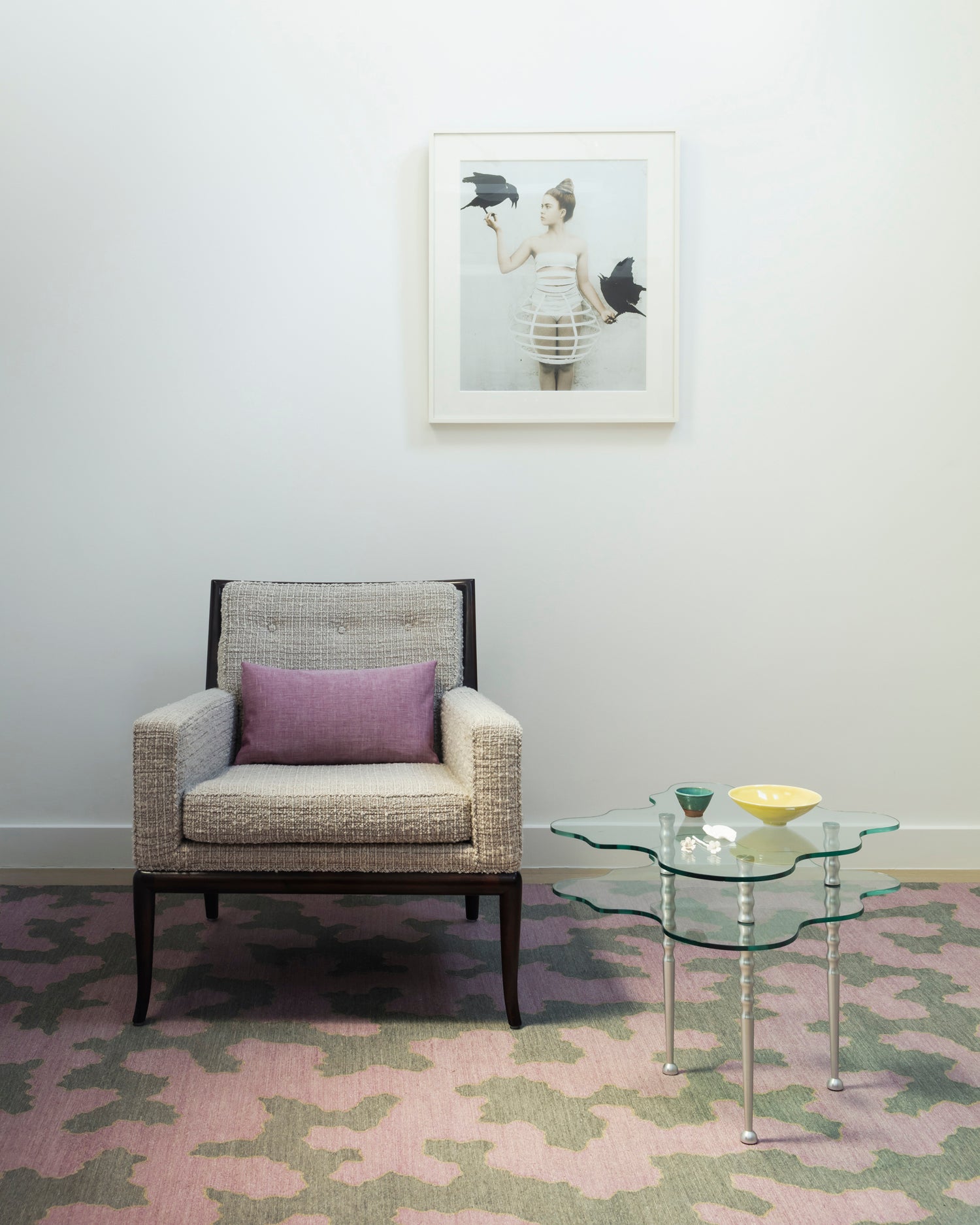 Side chair in white bouclé against a wall with atop a andwoven rug in an abstract coral design grey and purple with a tan accent line, with an organic cloud shaped side table with orange metal legs. 