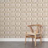 A wooden chair stands in front of a wall papered in a large-scale checked pattern in shades of brown and white.