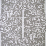 Detail of fabric in a large-scale tree and leaf print in white on a light gray field.
