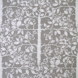 Detail of fabric in a large-scale tree and leaf print in white on a light gray field.