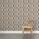 Side view of a wooden chair with woven seat on concrete floor against wallpaper in a large-scale checked pattern in shades of charcoal and pale grey.