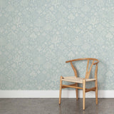 A wooden chair stands in front of a wall papered in a playful animal and tree print in white on a light blue field.
