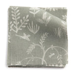 A stack of fabric swatches in a playful animal and tree print in white on a sage field.