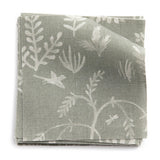 A stack of fabric swatches in a playful animal and tree print in white on a sage field.