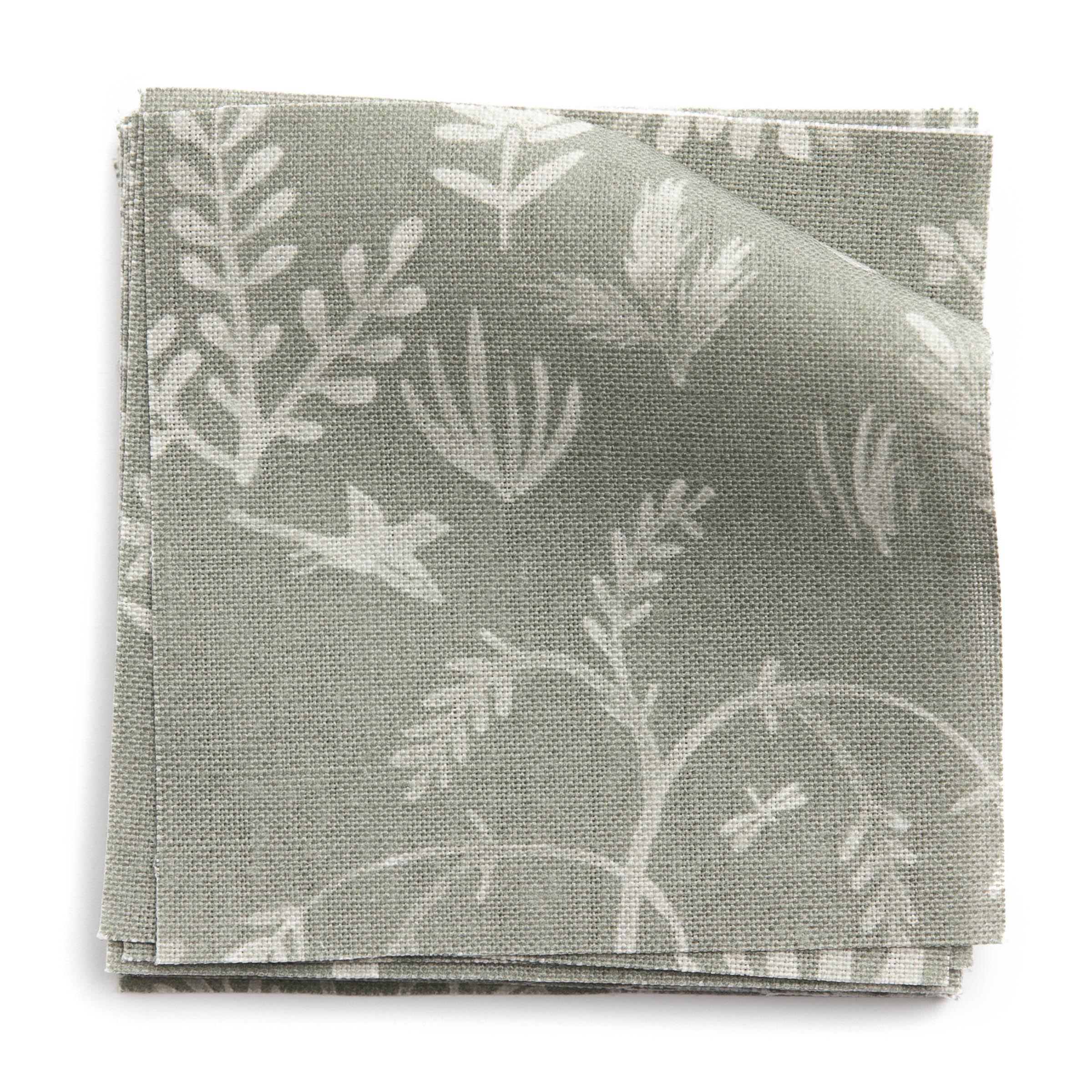 A stack of fabric swatches in a playful animal and tree print in white on a sage field.