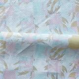 Draped fabric with painterly tropical checkerboard design in aqua blue, pink and tan.