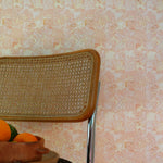 Chair with woven backrest against a tropical checkerboard patterned wall in pinky orange. 