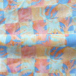 Draped fabric in a painterly tropical checkerboard design in blue, coral and orange. 